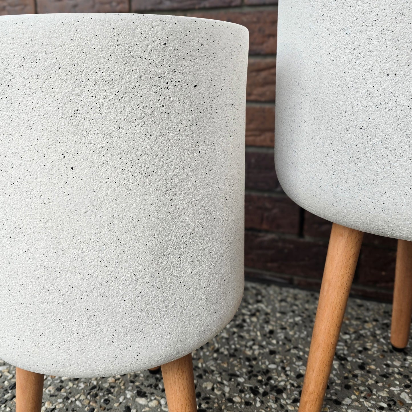 Close up picture of white indoor pot on wooden legs showing texture and detail of the pot, brick wall behind